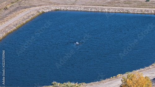 Aerial view of a dark blue reservoir with a small aerator in the center, surrounded by dry grassy terrain and a dirt path in Niwot, Colorado, United States.