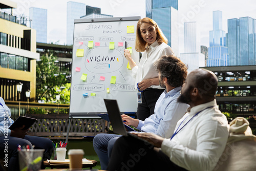 Businesswoman, whiteboard and growth strategy as presenter points at roadmap notes while colleagues follow discussion. Collaboration, project planning and decision making guide outdoor team workshop.