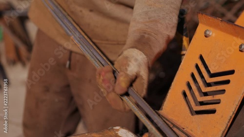 Worker feeding steel rebar into cutting machine close up