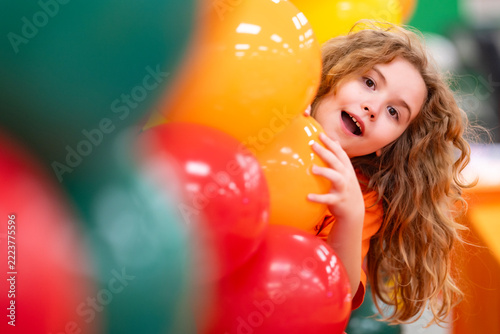 Festive balloons frame a smiling child. Festive decoration fills the bright background. Happy kid enjoys the festive event. Colorful balloons strengthen the festive portrait.