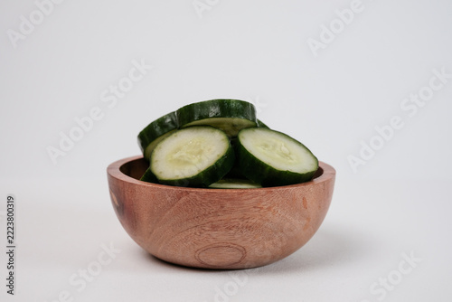 Cucumber slices sit in a wooden bowl. Fresh, green, crisp, and inviting. Simple background highlights natural textures. Perfect for healthy eating or wellness themes