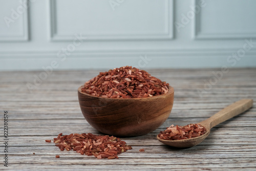 Red rice grains fill a rustic bowl and spoon. Wooden textures add warmth to the scene. Natural light highlights each grains rich hue. Ideal for health, nutrition, or cultural food themes