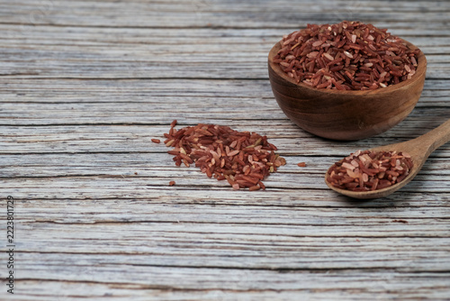 Red rice grains fill a rustic bowl and spoon. Wooden textures add warmth to the scene. Natural light highlights each grains rich hue. Ideal for health, nutrition, or cultural food themes