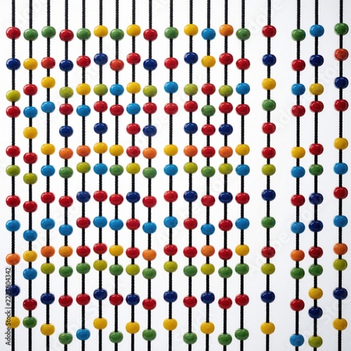 Colorful round beads hang on vertical black strings against white background. Many bright multicolor jewelry accessories create pattern. Rows of small plastic glass spheres display vivid rainbow