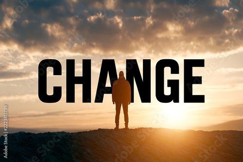 Silhouette of a person stands before a large word reading change at sunset