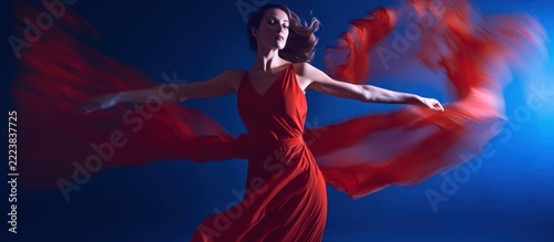 Graceful Woman in Red Dress Dancing with Flowing Fabric Against Blue Background.