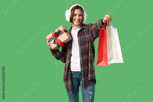 Beautiful young happy woman with shopping bags and gift box on green backgrou...