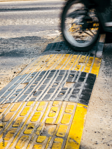 Motorcycle Wheel Crossing a Yellow and Black Speed Bump on Rough Asphalt Road

