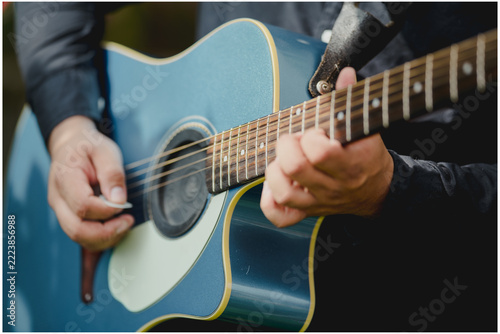 Obraz na plátně Close-up of a musician's hands playing a blue acoustic guitar, highlighting the strings, sound hole and finger placement on the fretboard