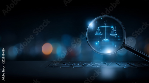 A magnifying glass displaying the scales of justice above a laptop illustrates legal research and digital compliance monitoring.