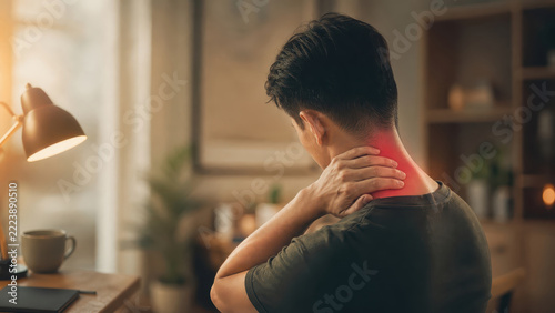 Man sitting at home desk rubbing painful neck from chronic muscle strain