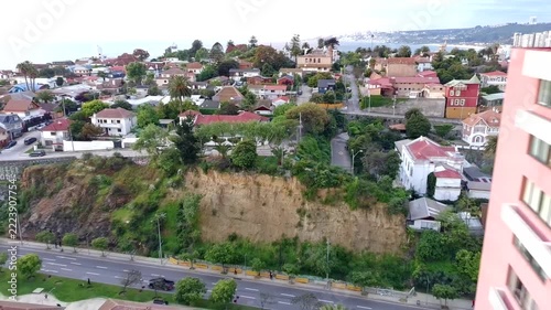 Aerial drone footage of a coastal residential neighborhood in Vina del Mar, Chile, featuring hillside houses, green vegetation, urban streets, apartment buildings and Pacific Ocean views.