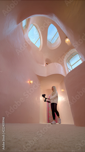 Recording a walking monologue with gimbal in a luxury hallway of soft pink curves and natural light architecture meets content