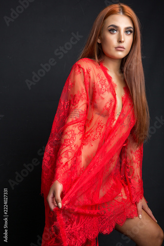 A model in a red lace robe with long red hair is posing in the studio. The dark background emphasizes the bright red color. 