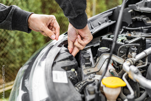 Person adjusting components inside car engine compartment under hood