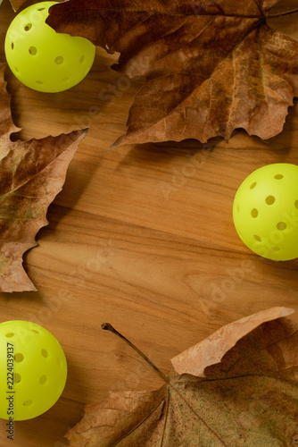 Yellow Pickleball Balls and Dry Autumn Leaves on Wooden Background