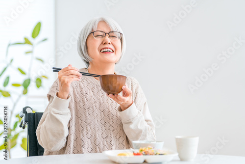 自宅のダイニングで美味しそうにお味噌汁を飲む車椅子ユーザーのシニア女性