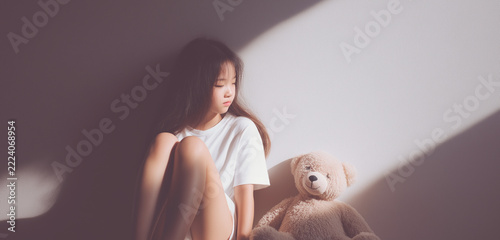 Asian girl sitting with teddy bear by wall, feeling lonely, sad, and reflecting on solitude