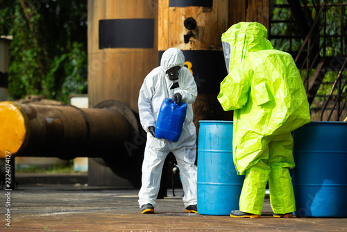 Hazmat specialists pouring chemical liquid into storage barrel