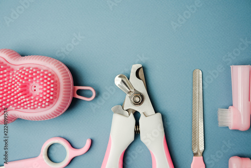 Pink pet grooming tools including clippers, brush, file, and finger toothbrush on blue backdrop.