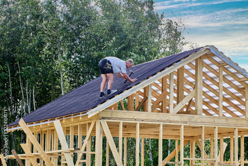 Asphalt roofing panels positioned by construction worker on triangular roof frame.
