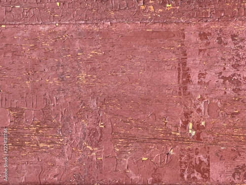 Weathered wooden plank with peeling red paint revealing yellow and brown wood grain and cracked flaking surface texture indicating aged rustic finish and layered brush strokes - close-up view.