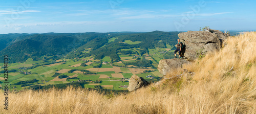Panoramic view of female hiker standing on granite rock outcrop overlooking vast countryside valley in Austria