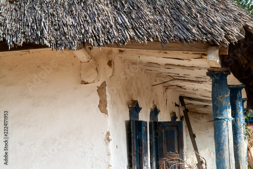 Architectural corner detail of thatched roof overhang and wooden porch columns on old clay house