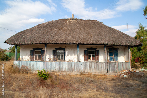 Traditional Ukrainian thatched roof mud hut with wooden porch and blue shutters in rural landscape