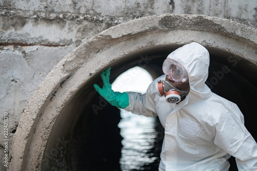 Worker In Protective Suit Inspecting Urban Sewer Manhole.