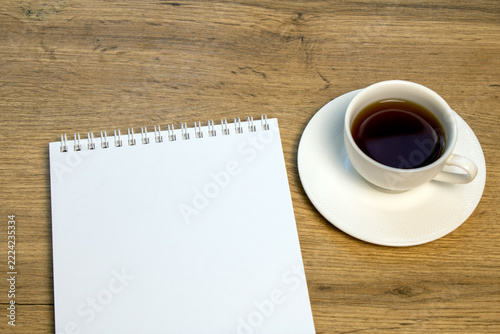 Blank white notepad and a cup of black coffee on a wooden desk. Daily planning and productivity concept with copy space.