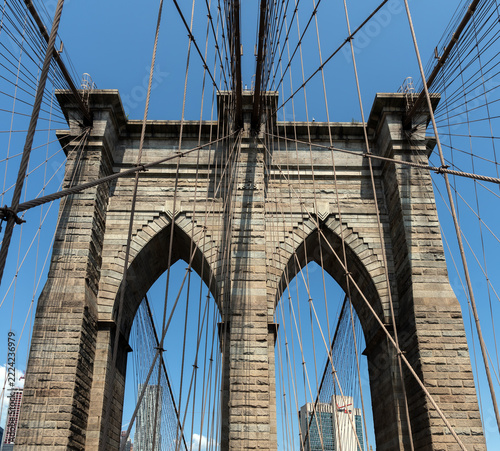 2019 New York City, USA; Architectural detail of the stone tower of the Brooklyn Bridge with gothic arches, steel suspension cables, year 1875 plaque