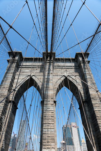 2019 New York City, USA; Architectural detail of the stone tower of the Brooklyn Bridge with gothic arches, steel suspension cables, year 1875 plaque