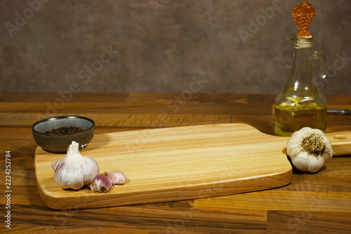 Wooden Cutting Board With Garlic, Black Pepper and Olive Oil on Rustic Kitchen Counter
