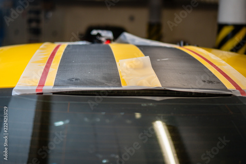 Close-up of a yellow sports car roof during racing stripe installation, showing black vinyl wrap with transfer tape in the process of vehicle customization
