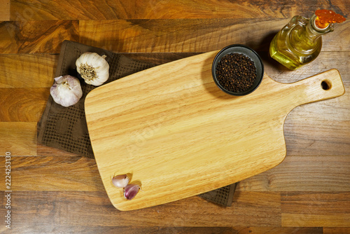 Wooden Cutting Board With Garlic, Black Pepper and Olive Oil on Rustic Kitchen Counter