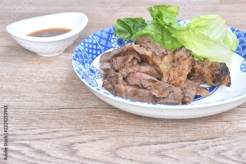 grilled slice salty beef meat with cos lettuce salad on plate dipping spicy chili sauce in cup