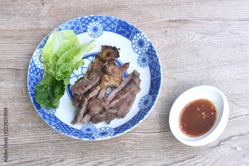 grilled slice salty beef meat with cos lettuce salad on plate dipping spicy chili sauce in cup