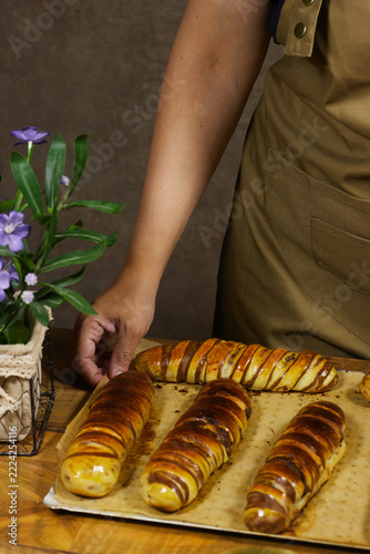 Baker Arranging Fresh Golden Braided Bread on Tray at Rustic Kitchen Table