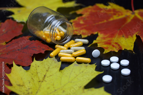 Pills and maple leaves, bottle of capsules and scattered tablets. Concept of nutrition supplements, antidepressants, vitamins for immunity in autumn flu season