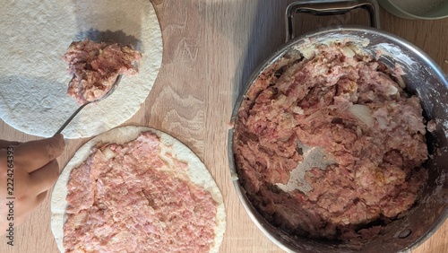 Obraz na plátně hand using a spoon to spread raw minced meat onto round flatbreads or tortillas