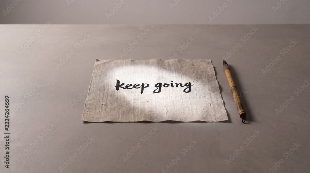 Naklejka premium Motivational Keep Going Text Written in Black Ink Calligraphy on Textured Fabric with Bamboo Brush on Grey Background Wide Context Minimalist Concept