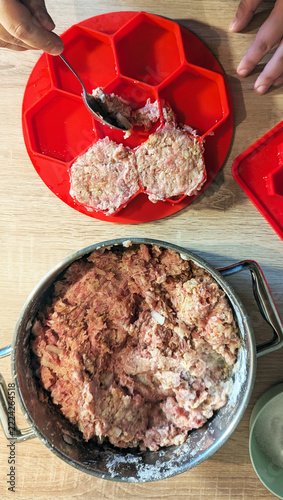 Fotografie hand using a metal spoon to pack raw minced meat into large red silicone hexagon