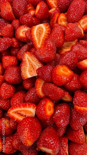 A vibrant collection of juicy, red strawberries, some halved to reveal their fresh interiors. The glossy texture highlights their freshness and appeal.
