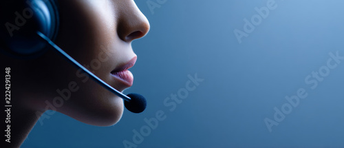 A woman wearing a headset with the microphone close to her mouth, against a blue background