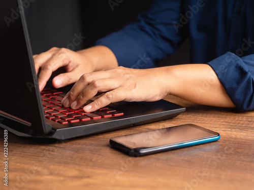 Person typing on laptop with smartphone on desk