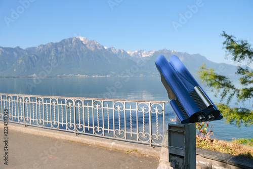 Coin operated binocular viewer by lakeside railing with alpine backdrop