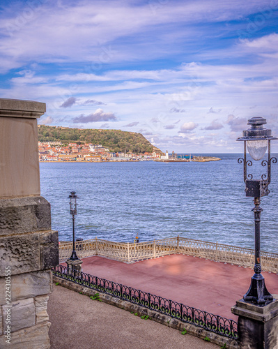 A seaside town with a castle wall on a hill and a streetlight in the foreground.