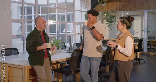 Diverse team on coffee break in office, left speaker leaning and gesturing with mugs