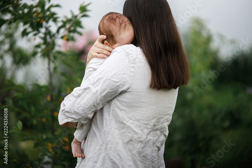 Mother kissing and hugging cute newborn baby in the garden, close up. Love, care and family in countryside concept. Happy Mothers day! Adoption and maternity